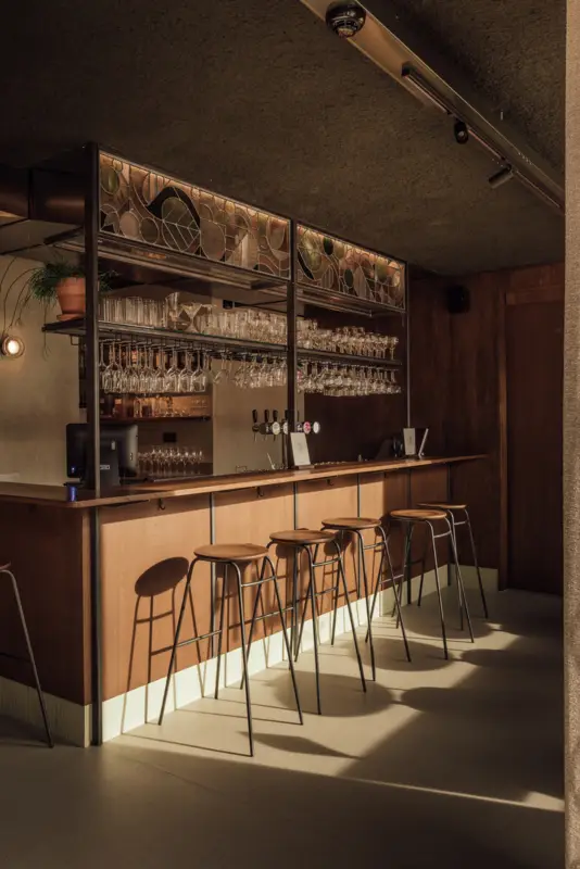 widok na otwarty bar w Tilii - reflektory Modular Minude Track 48V Adjustable akcentujące witraż i półki z butelkami - eetcafé Linden, Belgia